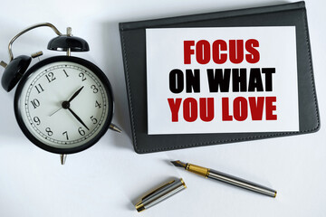 On the table there is a clock, a pen, a notebook and a card on which the text is written - FOCUS ON WHAT YOU LOVE