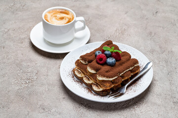 portion of Classic tiramisu dessert with raspberries, blueberries and cup of coffee on grey concrete background