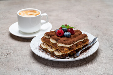 portion of Classic tiramisu dessert with raspberries, blueberries and cup of coffee on grey concrete background