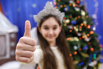 Happy little 10 years girl show thumb up, sign ok, looking at camera in christmas decorated home indoor
