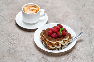 portion of Classic tiramisu dessert with raspberries and cup of coffee on grey concrete background