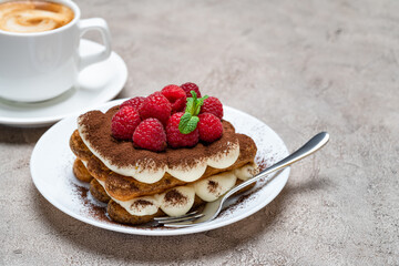 portion of Classic tiramisu dessert with raspberries and cup of coffee on grey concrete background