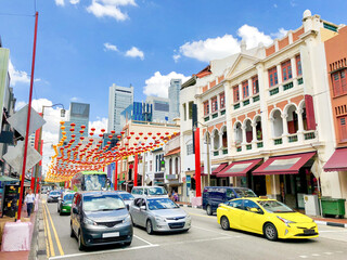 Street life and view in Chinatown in Singapore, Malaysia with traffic, cars, buildings, lanterns and Chinese shops and restaurants with city skyline on summer day with blue sky