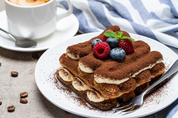 portion of Classic tiramisu dessert with raspberries, bluebedrries and cup of coffee on grey concrete background