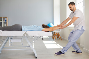 Man chiropractor or osteopath stretching woman patients arms and back during visit in manual...
