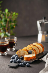 Sweet roll with cream and blueberries on a board on a dark background