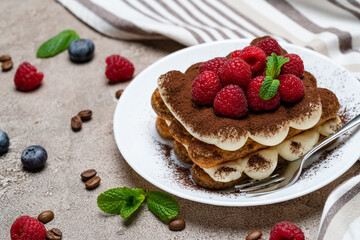 portion of Classic tiramisu dessert with raspberries and blueberries on grey concrete background