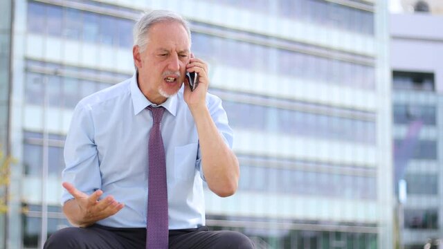 Angry businessman yelling at the phone outdoor sitting no a bench
