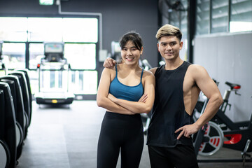 Fototapeta na wymiar Cheerful healthy Asian sportspeople portrait in a gym with copyspace. Asian young sportswoman and sportsman posing for a photography in a indoor gym. Wellness and wellbeing in healthy people concept.
