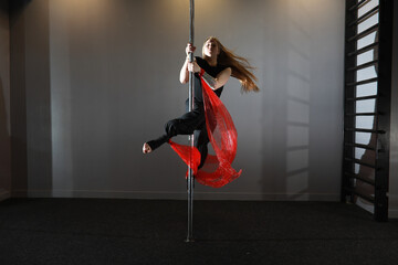 The dancer on the pylon in the studio. Girl doing exercises on a sports equipment.