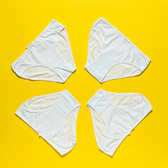Set of four white women's panties on a bright yellow background. Flat lay.