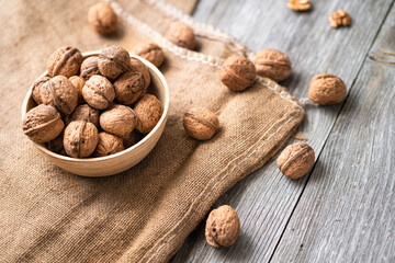 Whole walnuts in a bowl and jute bag on rustic old wooden table. Healthy organic food, BIO viands, natural background. Copy space for your advertising text message