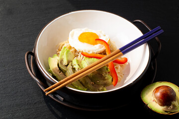 Healthy food concept Asian homemade avocado rice noodles and fried egg on black slate stone with copy space