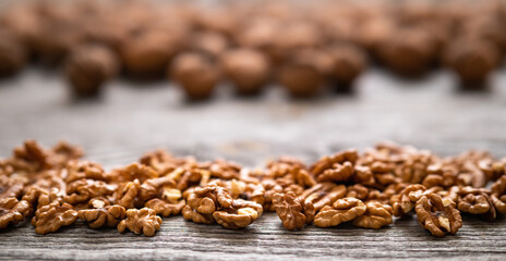 Heap of fresh walnut kernels and whole walnuts on wooden table - natural pattern background detail. Close up of brown surface texture. Healthy organic food, BIO viands, back to nature concept