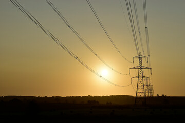 Fototapeta na wymiar National Grid power lines lead to a row of electricity pylons silhouette at sunrise in Buckinghamshire.