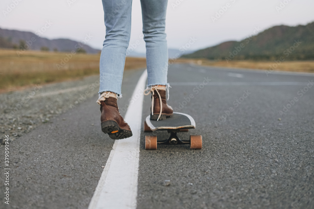 Wall mural Crop photo of women's legs in jeans on longboard on road with the mountains background - Wall murals