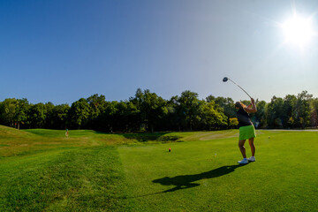 wide shot female golfer sunny golf course swinging driver on tee