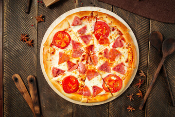 Pizza with ham and tomatoes on the wooden table