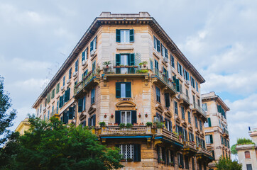 Fototapeta na wymiar Rome, Italy - A beautifully architectured apartment in downtown Rome during a cloudy afternoon with the classical green windows and outdoor plants positioned below the windows