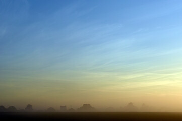 Dawn mist with wispy clouds and light blue sky fading to orange over the village of Bishopstone in Buckinghamshire