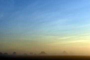 Obraz premium Dawn mist with wispy clouds and light blue sky fading to orange over the village of Bishopstone in Buckinghamshire