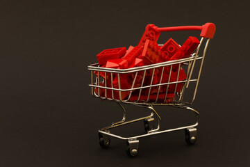 mini supermarket cart filled to the brim with red blocks on a black background, color contrast....