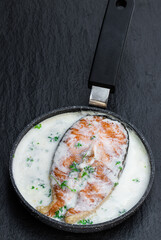 Fresh salmon steak in in cream sauce on black stone background