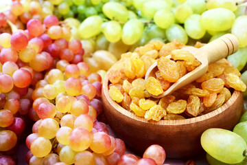 Dried yellow raisins in wooden spoon with fresh ripe grapes, selective focus