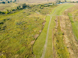 Fototapeta na wymiar Dirt road among green meadows. Summer sunny day. Aerial drone view.