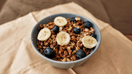 Close up of homemade granola in a plate with nuts, honey, blueberries, banana and other natural ingredients served on napkin