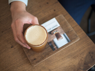 Top view of man's hand hold a glass of coffee on wooden plate in cafe.(Selective focus)
