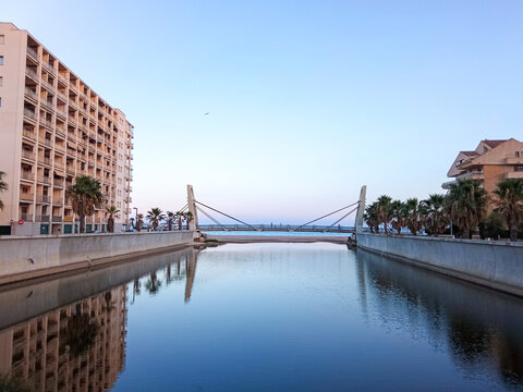 Rio con edificios a los lados con reflejo, puente al fondo y cielo despejado
