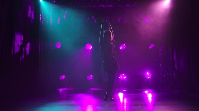 A young woman in a black short dress is dancing rumba elements against a background of purple lights. Slow motion.