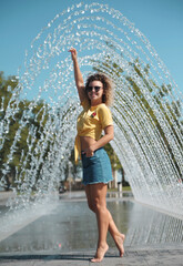 Smiling young woman has fun in fountain outdoors. Cozy autumn.