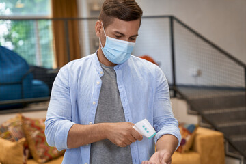 Young male office worker wearing medical protective mask standing in the office and checking...
