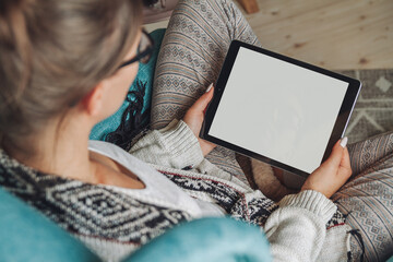 woman sitting in cozy armchair, with warm blanket, using tablet