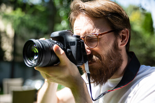 A young bearded man taking pictures outdoor with a professional digital camera.
