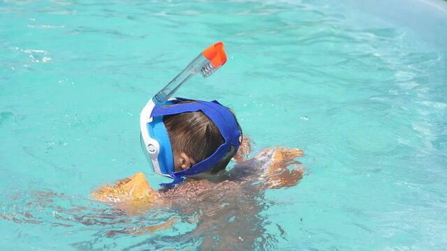Happy boy in armbands and water mask swims under water in the pool. Summer holidays.