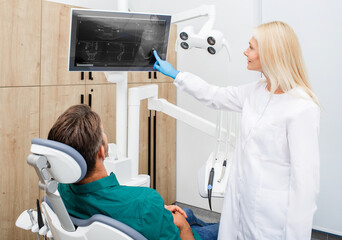 Beautiful woman dentist consulting a man patient, patient has a wisdom tooth ache. Treatment or...