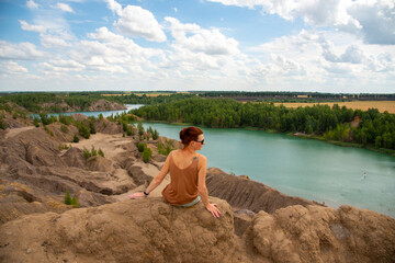 Naklejka na ściany i meble A woman with red hair and dark glasses sits on a high mountain above a bright blue lake .