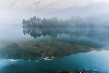 lake with reflection of mountains in fog