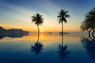 Fototapeta na wymiar Silhouette of coconut trees agains sunrise off of the sea