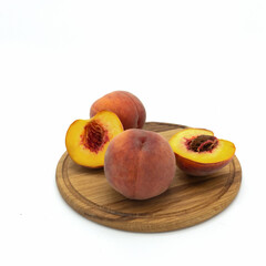 Fototapeta na wymiar Ripe fresh peaches on a round wooden board. Two fruits are whole, one is cut in half. Side view. Isolated over white background.