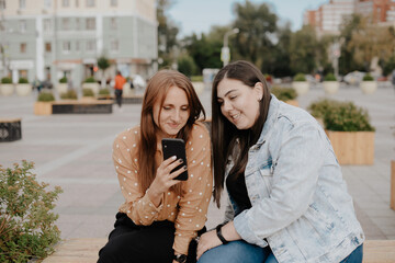 Two young women sit in a city Park with a phone