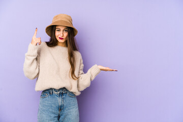 Young caucasian woman isolated on purple background holding and showing a product on hand.