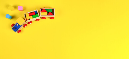 Wooden toy train with colorful blocks on yellow background. Top view