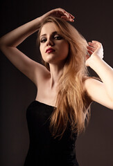 Beautiful natural makeup woman with long blond hair style in black dress, red lipstick and epilation armpits looking on black background.. Closeup