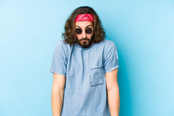 Young long hair man wearing a festival hipster look isolated shrugs shoulders and open eyes confused.