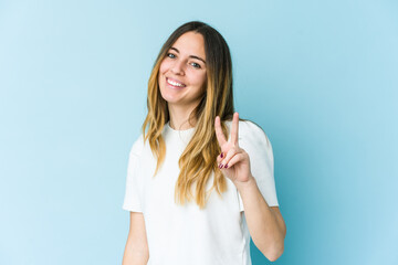 Young caucasian woman isolated on blue background showing victory sign and smiling broadly.