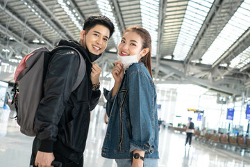 Asian man and woman wearing protective mask in airport terminal for social distancing. new normal friend or couple lifestyle with backpack ready to travel. happy smile face and enjoy for trip 